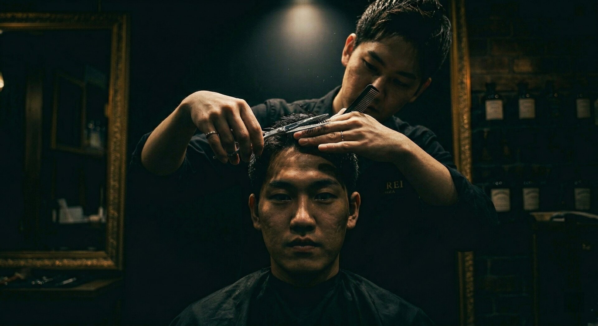 Male barber cutting a customer's hair in a dark teal salon with mirrors and moody lighting